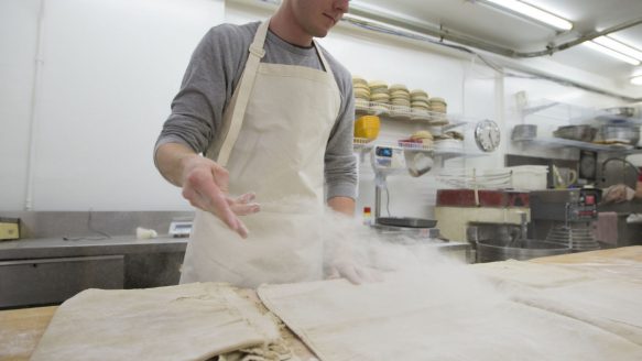 Baker Spencer Smith dusts work surfaces with flour before getting ready to work with the bread dough. St. John Bakery transforms lives with job training and the simple alchemy of bread, yeast and water.